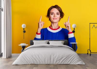 Photo portrait of lovely young lady point up empty space dressed stylish blue knitted garment isolated on yellow color background Wall mural