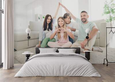 Photo portrait of parents showing roof with hands over heads and children sitting on carpet little daughter showing heart sign Wall mural