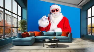 Photo portrait of retired old man hold point door key service dressed stylish santa claus costume coat isolated on blue color background Wall mural