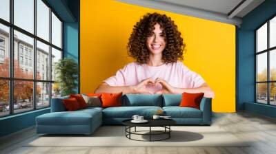 Photo portrait of romantic girlfriend with curly hairstyle demonstrating love symbol heart isolated on vivid yellow color background Wall mural