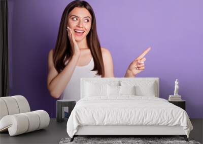 Photo portrait of smiling girl touching face with one hand pointing finger at blank space isolated on vivid purple colored background Wall mural