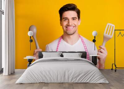 Photo portrait of smiling guy holding kitchenware isolated on vivid yellow colored background Wall mural