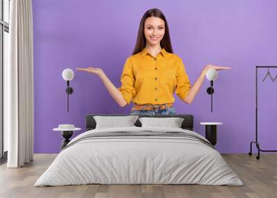 Photo portrait of smiling woman keeping blank space on hands comparing isolated on pastel violet color background Wall mural