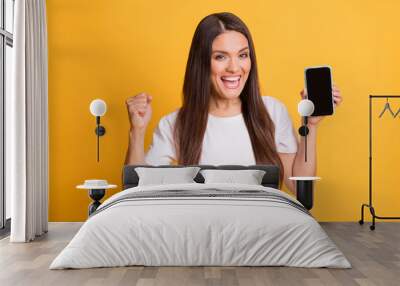 Photo portrait of woman showing smartphone touchscreen with copyspace gesturing like winner isolated on bright yellow color background Wall mural