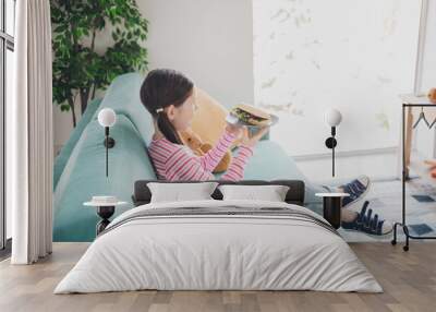 Photo portrait of young funny kid little brunette girl staying at home hungry eating yummy tasty baguette sandwich isolated in her room Wall mural