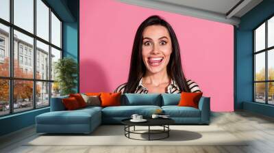 Playful young woman with brunette hair making a silly face in a casual striped shirt against a vibrant pink background Wall mural