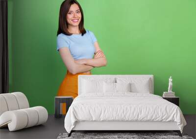 Portrait of adorable satisfied girl beaming smile folded arms empty space isolated on green color background Wall mural