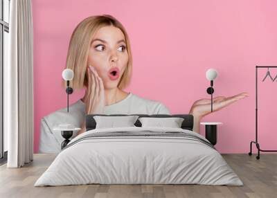 Portrait of astonished girl with bob hairstyle wear white t-shirt staring at product on arm empty space isolated on pink color background Wall mural