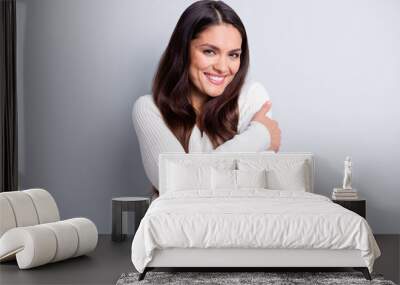 Portrait of attractive cheerful brown-haired girl embracing herself soft clothes isolated over grey pastel color background Wall mural