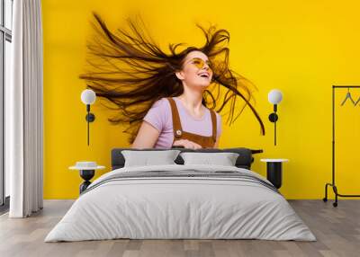 Portrait of attractive cheerful dreamy girl riding scooter air blowing having fun good mood isolated over bright yellow color background Wall mural