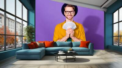 Portrait of attractive cheerful guy holding in hands fan cash dollars spend isolated over bright violet purple color background Wall mural