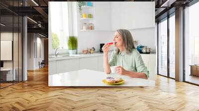 Portrait of attractive elderly dreamy grey-haired woman drinking coffee eating yummy tasty bakery at home light white indoors Wall mural