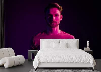 Portrait of attractive serious content guy wearing t-shirt isolated over dark neon light violet color background Wall mural