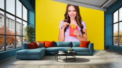 Portrait of charming slim cheerful wavy-haired girl eating french fries leisure isolated bright yellow color background Wall mural