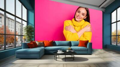 Portrait of charming youth hugging herself looking with beaming smile wearing yellow pullover isolated over fuchsia background Wall mural