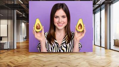 Portrait of cheerful nice girl beaming smile arms hold two halves avocado isolated on purple color background Wall mural