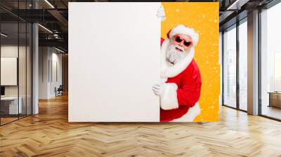 Portrait of funny funky christmas father in red hat headwear look behind white wall poster advertise winter x-mas shopping seasonal miracle sales discounts isolated over bright color background Wall mural