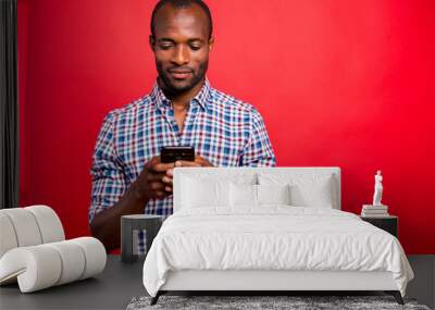 Portrait of he nice handsome attractive cheerful guy wearing checkered shirt holding in hands cell playing game isolated over bright vivid shine red background Wall mural