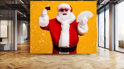 Portrait of his he nice attractive cheerful cheery glad fat overweight Santa holding in hand usd 100 salary deposit bank card isolated bright vivid shine vibrant yellow color background Wall mural