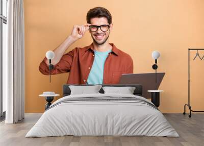 Portrait of his he nice attractive cheerful cheery successful content brunette guy holding in hands laptop working part-time touching specs isolated over beige color pastel background Wall mural