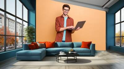 Portrait of his he nice attractive cheerful cheery successful content smart clever brunet guy agent broker holding in hands laptop working isolated over beige color pastel background Wall mural