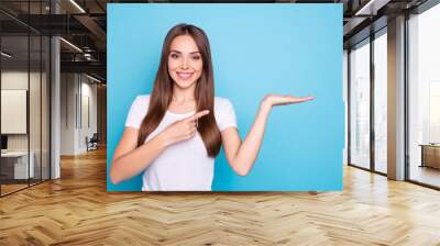 Portrait of lovely millennial holding hand pointing to ads with her index finger isolated over blue background Wall mural