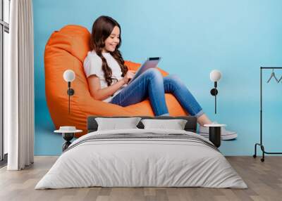 Portrait of nice attractive cheerful cheery focused wavy-haired girl sitting in chair using tablet ebook isolated on bright vivid shine vibrant blue teal turquoise color background Wall mural