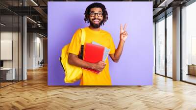 Portrait of nice impressed brunet guy hold books show v-sign wear spectacles bag orange t-shirt isolated on vibrant lilac background Wall mural