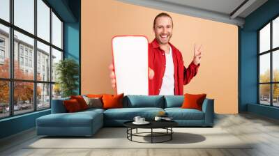 Portrait of nice young man show empty space screen wear red shirt isolated on beige color background Wall mural