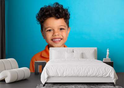 Portrait of positive cheerful kid boy smiling on camera isolated over blue color background Wall mural