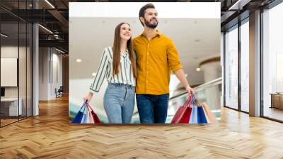 Portrait of positive cheerful spouses man woman wife husband have enjoy fun free time in shopping center mall hold many packages bags wear striped yellow shirt denim jeans Wall mural