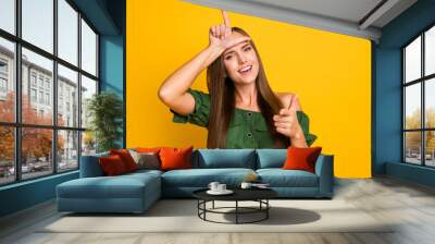 Portrait of pretty cheerful brown-haired girl bullying pointing at you showing horn sign isolated over bright yellow color background Wall mural