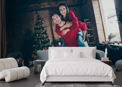 Portrait of romantic two youth hug piggyback on christmas x-mas party event wearing red jumper denim jeans in house with decoration illumination lights indoors near couch Wall mural