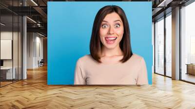 Portrait of satisfied adorable person beaming smile tongue lick teeth isolated on blue color background Wall mural