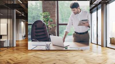 Portrait of serious concentrated middle eastern chief man leader economist working on computer hold tablet send emails to startup partners stand near window in loft Wall mural