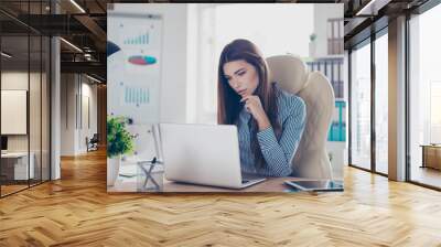 Portrait of serious young businesswoman in formal wear, sitting at her work place and concentrated on data in the laptop Wall mural