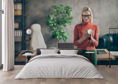 Portrait of smart company owner woman use smartphone chatting with employees colleagues stand near wooden table in office loft wear red turtlneck Wall mural