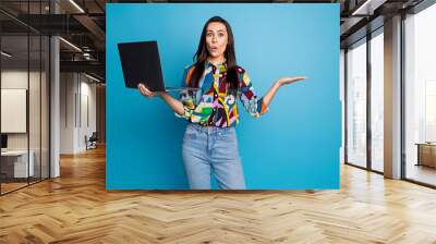 Portrait of speechless girl with straight hair holding laptop palm presenting object empty space isolated on blue color background Wall mural