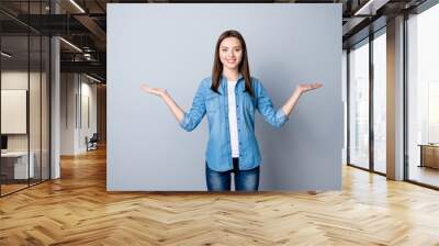 Portrait of successful cheerful cute young woman presenting something, showing copy space on her palm in two sides, looking at camera, standing over grey background Wall mural