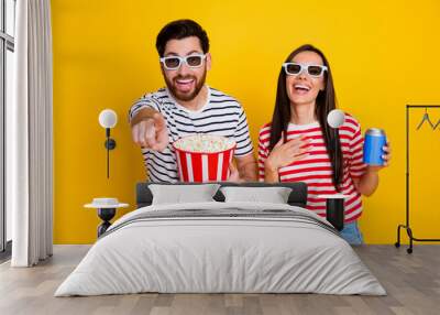 Portrait of two crazy cheerful people watch movie 3d glasses hold popcorn soda drink finger point you isolated on yellow color background Wall mural