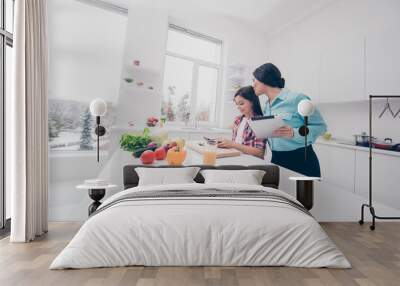 Portrait of two nice lovely sweet attractive adorable cheerful cheery kind people mommy mom kissing girl making salad in light white kitchen interior Wall mural