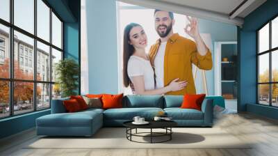 Portrait of two young people cuddle show okey symbol eye wink weekend pastime modern interior flat indoors Wall mural