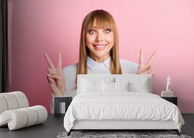 Portrait of young cheerful positive good mood smiling attractive woman showing v-sign isolated on pink color background Wall mural