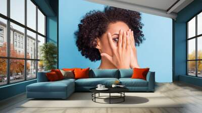 Portrait of young scared afraid frightened african girl cover face with hands stressed isolated on blue color background Wall mural