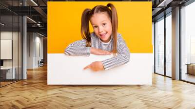 Portrait of young smiling cheerful little girl child kid pointing finger on white poster banner isolated on yellow color background Wall mural