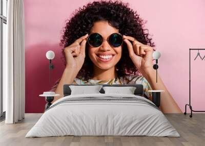 Portrait photo of black skinned curly woman wearing round stylish sunglass smiling isolated on pastel pink color background Wall mural