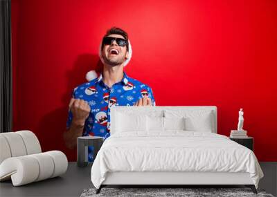 Portraitof satisfiec man dressed christmas hat blue shirt in sunglass clenching fists win lottery isolated on vivid red color background Wall mural