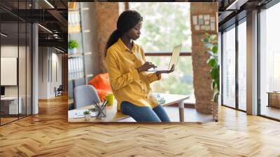 Profile side photo of concentrated afro american business woman sit on table browse internet laptop in office indoors workplace Wall mural