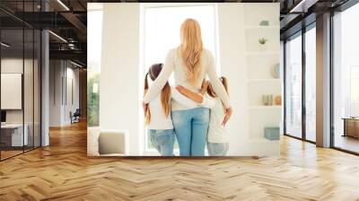 Rear back behind view of nice stylish trendy slim people mom mum girls hugging in front of window in light white interior room hotel indoors Wall mural