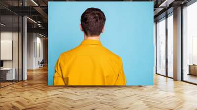 Rear behind view photo of brunette guy standing turned back not showing face ignoring speaking to girlfriend wear yellow shirt isolated blue color background Wall mural